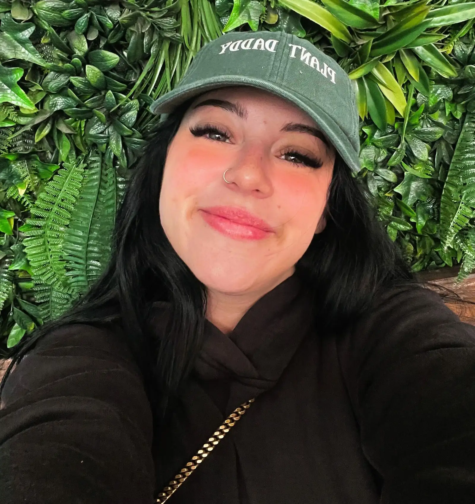 Haley Quinn smiling in a green cap in front of a leafy wall